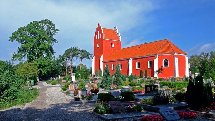 Rødt kirke med gravhøje og blomsterbænke i forgrunden