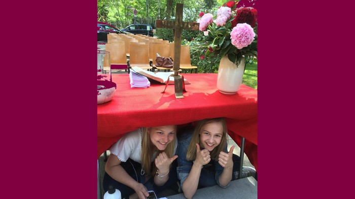 Zwei Mädchen sitzen unter einem Tisch und lächeln.