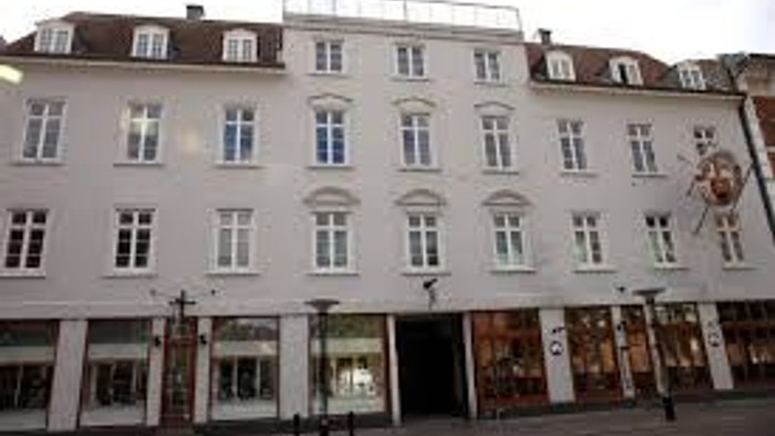 Et stort, hvide bolig- og butikshus med mange vinduer og en central indgang.