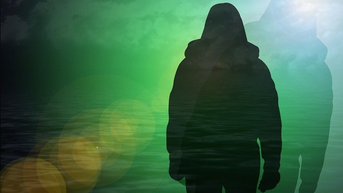 Eine dunkle Gestalt steht vor einem leuchtenden, grünen Hintergrund.