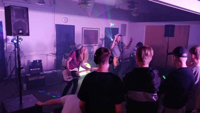 En liveband optræder på en lille scene foran et publikum.