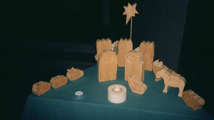 Holzfiguren von Maria, Josef, Baby Jesus und Tieren auf grünem Tisch