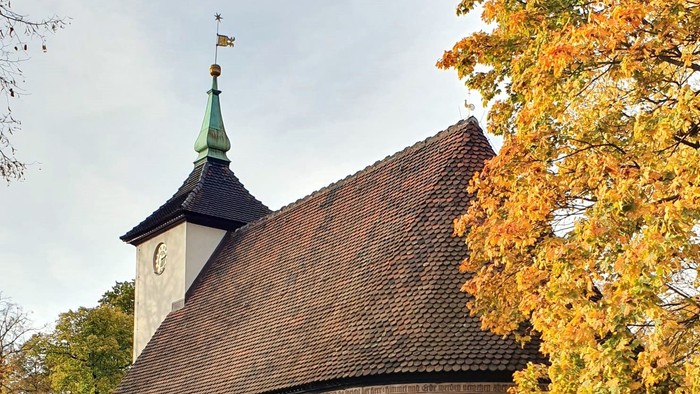 Kleine Kirche mit Uhrturm und spitzem Dach, umgeben von Herbstbäumen