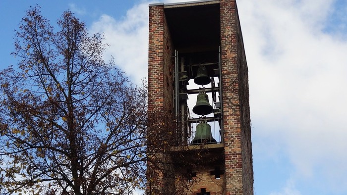 Ein hoher Ziegelbau mit Uhr und leerer Fensterhöhle vor blauem Himmel und Baum.
