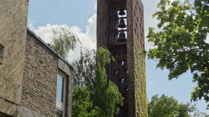 Ein hohes, verwittertes Ziegelgebäude mit einem offenen Turm und umgebenden Bäumen