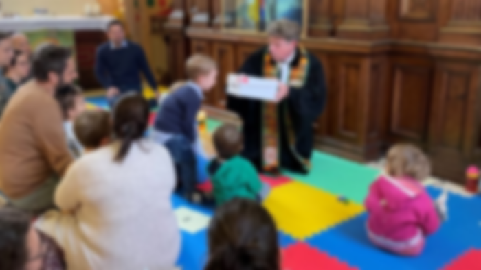 Kinder spielen auf bunten Matten in einem Raum mit Erwachsenen.