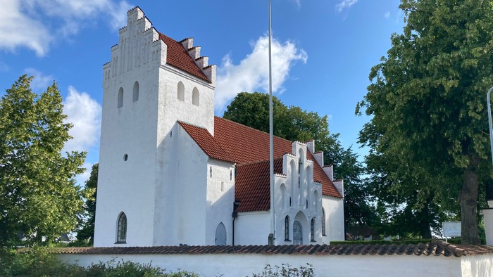 Et hvidt kirkebygning med røde tag og en tårn med en flaggstang.