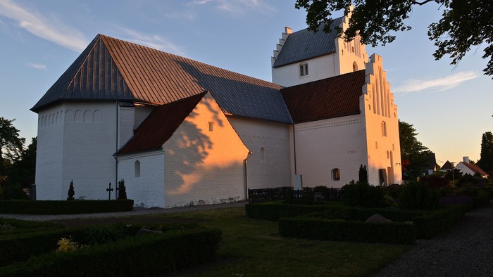 En lille, hvid kirke med rødt tag og tårn ved solnedgang