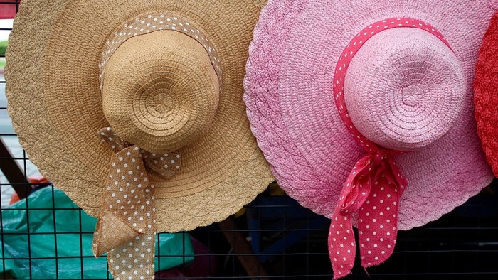 Drei Strohhüte mit bunten Bändern hängen an einem Zaun