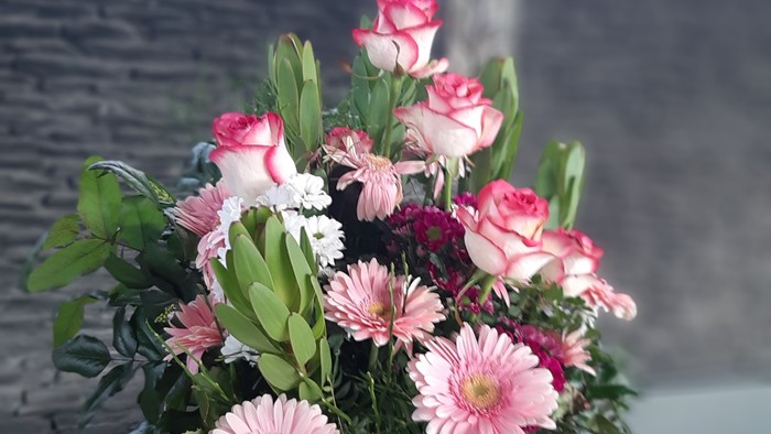 Blumenstrauß in Vase vor Kreuz an der Wand