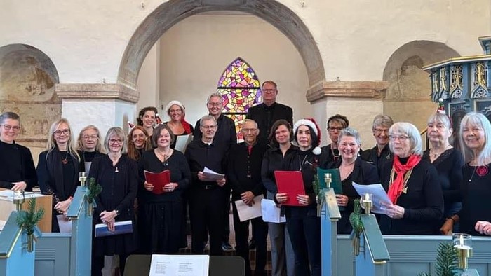 Gruppe af mennesker, der poser sammen i en kirke, nogle holder bøger og papirer.