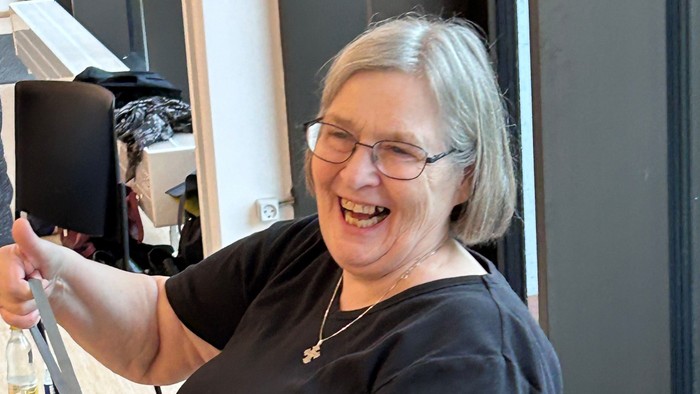 En kvinde med briller og halskæde sidder i en kantine og holder en kaffe-tasse.