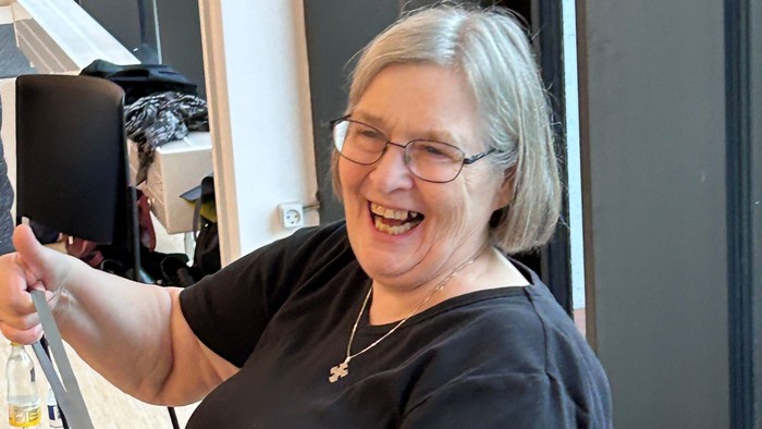 En kvinde med briller og halskæde sidder i en kantine og holder en kaffe-tasse.