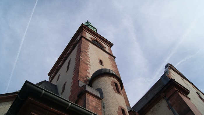 Hoher Ziegelturm mit grünem Dach vor blauem Himmel.
