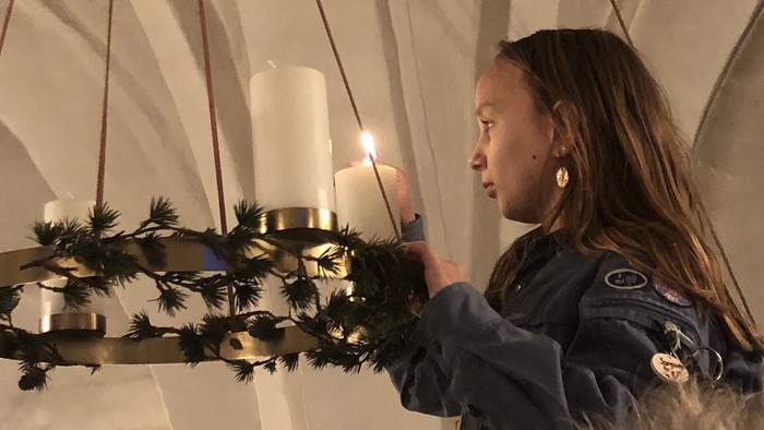 En kvinde tændes lys på en kransekage med lysstaker og grønne grenar.