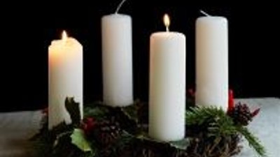 En adventskranse med fire tændte lys på en træstamme.