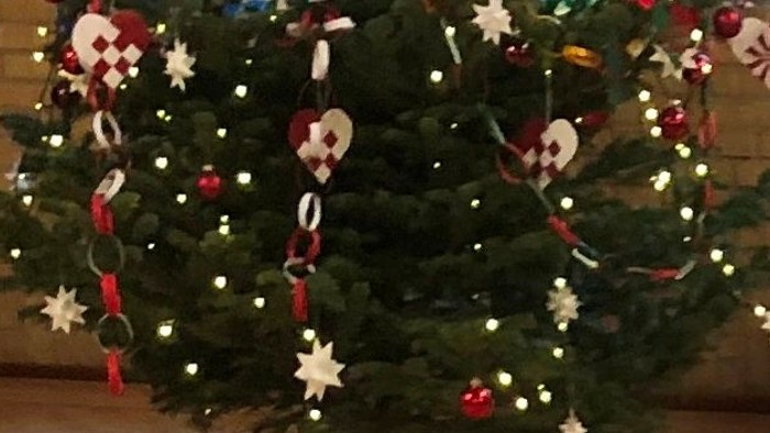 En festligt jul-bord med julerose, lyse, og pyntet juletree i baggrunden