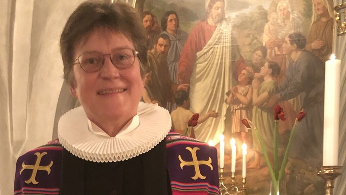 En kvinde i religiøs tøj står foran et alter med maleri.