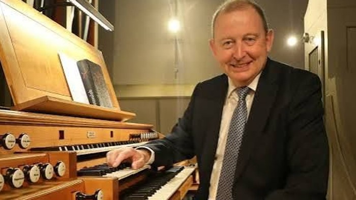 Ein Mann im Anzug spielt mit einem warmen, professionellen Lächeln eine komplexe Pfeifenorgel.