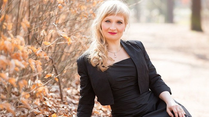 Eine Frau in schwarzem Kleid sitzt im Herbstlaub.