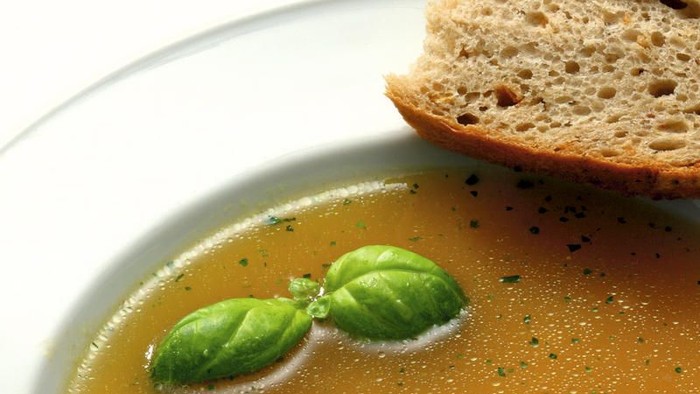 Eine Schale Suppe mit Basilikum und ein Stück Brot