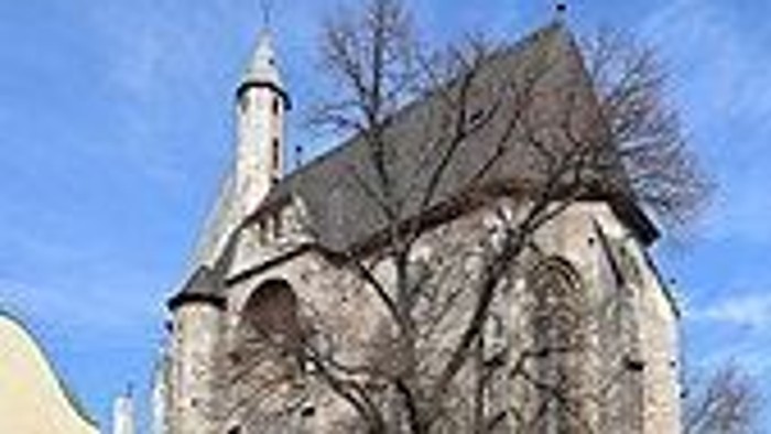 Historische Steinkirche mit hohem Turm und angrenzenden Wohngebäuden unter klarem blauem Himmel.