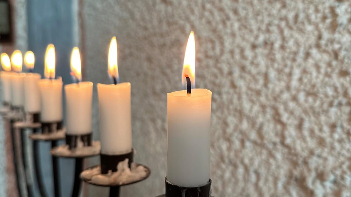 Mehrarmiger Kerzenleuchter mit brennenden Kerzen vor texturierter Wand