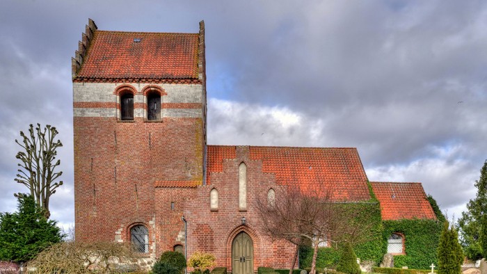 En rød murstenskirke med spiret og gravhøje i forgrunden
