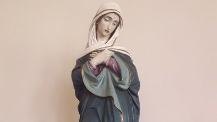 Die Statue einer Frau in blauer Robe auf einem hölzernen Sockel