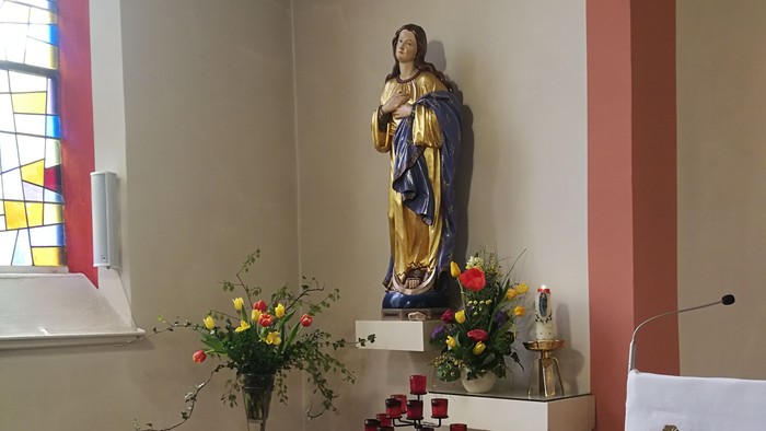 In der Kirche steht eine Statue der Jungfrau Maria mit Blumen und Kerzen.