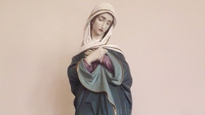 Die Statue einer Frau in blauer Robe auf einem hölzernen Sockel