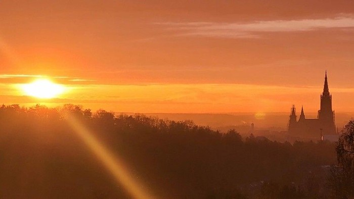 Sonne geht über Stadt mit Kirche unter orangefarbenem Himmel