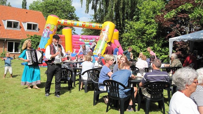 En fest med folk, der sidder ved bord og ser en show med to dansere og en bouncy castle i baggrunden