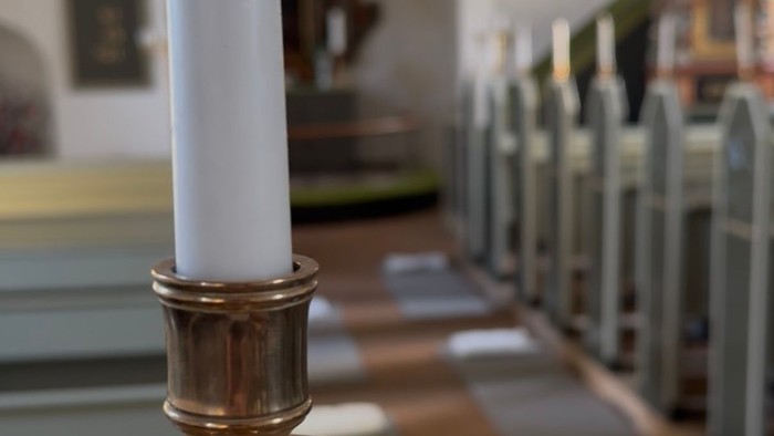 Et stearinlys i en messinglysestage på et bord i en kirke.