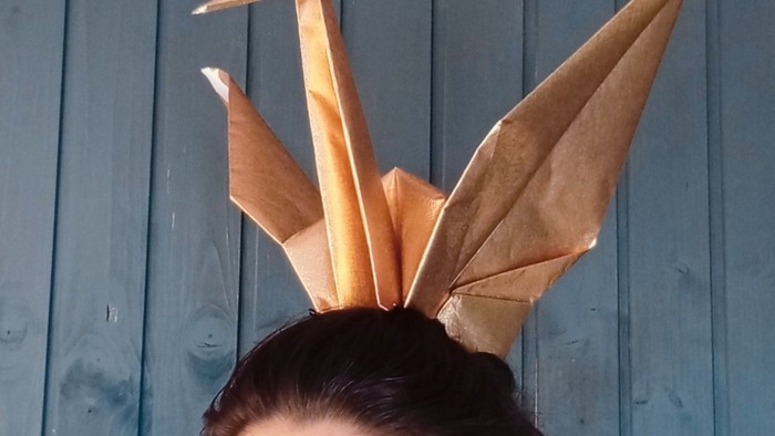 Frau mit Origami-Kranich-Kopfschmuck vor blauem Holzzaun