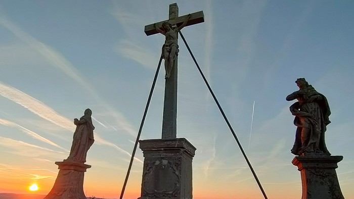 Kreuz mit Statuen, Sonnenuntergang im Hintergrund