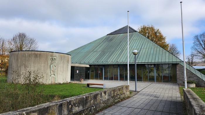 Modernes Gebäude mit grünem Dach und Glasfront, umgeben von Grünfläche und Bäumen