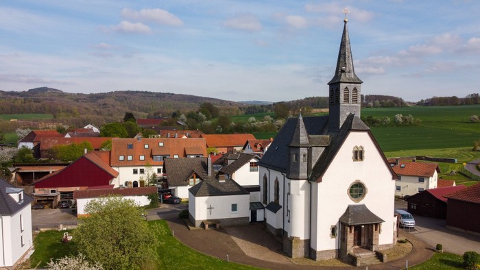 Luftaufnahme eines malerischen Dorfes mit einer markanten weißen Kirche mit hohem Kirchturm und umliegenden Häusern.