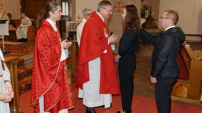 Eine Gruppe von Menschen in einer Kirche, einige in roten und weißen Gewändern, andere in formeller Kleidung.