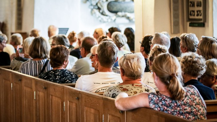En kirkefuld med mennesker, der sidder på bænke.