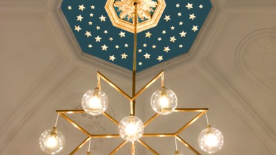 En stor belysning med glasskyer hænger fra et blå tak med stjerner og en midterstjerne.