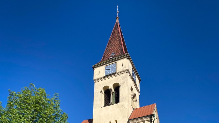 Eine historische Kirche mit einem hohen Glockenturm, einem gewölbten Eingang und grünen Türen vor einem klaren blauen Himmel.