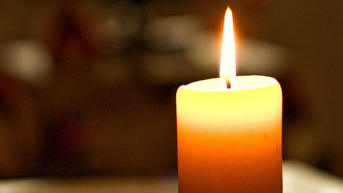 Kerze im Halter mit brennendem Docht, bunte Lichter im Hintergrund