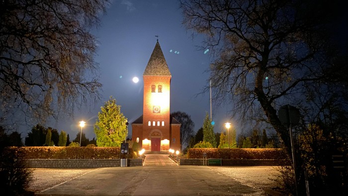 En lyset kirke med klokketårn og en person står foran den om natten