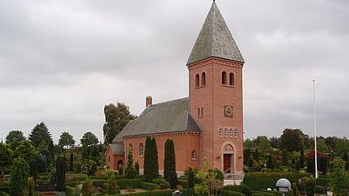 En rød kirke med højt tårn og en have med blomster.