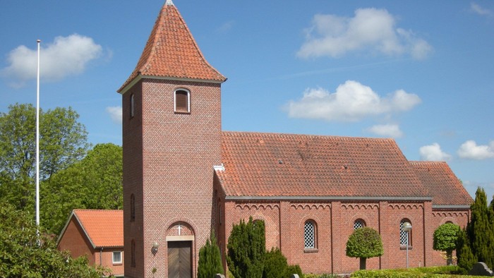 En rød murstenskirke med tårn og omgivet af grønne planter og blomster.