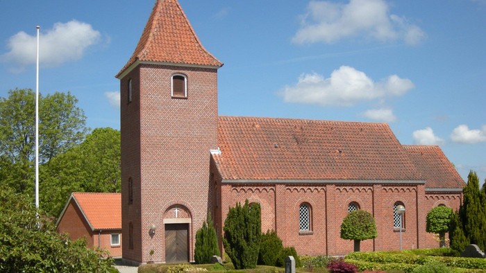 En rød murstenskirke med tårn og omgivet af grønne planter og blomster.
