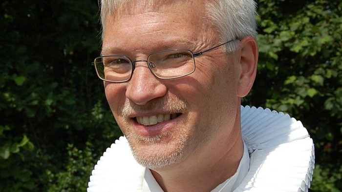 Mand med hvid krage og briller.