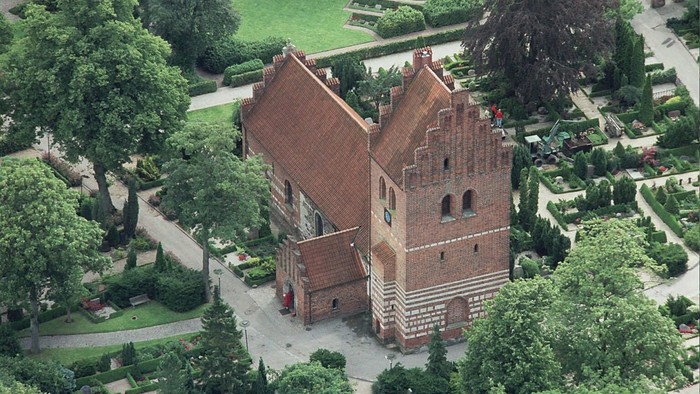 Historisk murstenskirke omgivet af frodige, velplejede haver og stier.