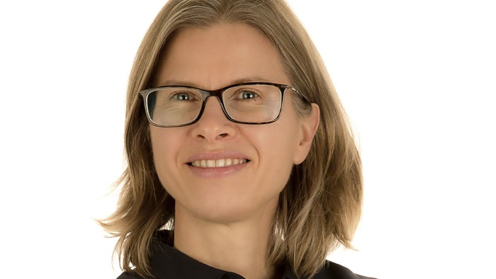 En kvinde med kort, blond hår og briller smiler til kameraet.